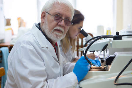 Health care researchers working in life science laboratory. Young female research scientist and senior male supervisor preparing and analyzing microscope slides in research lab.の写真素材