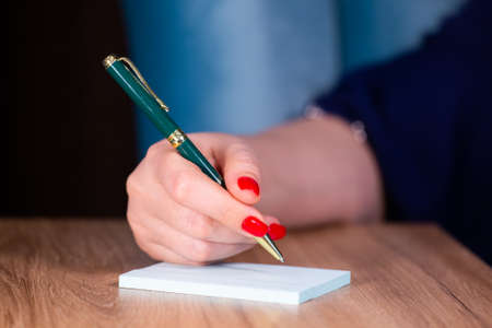 Beautiful female hand close up with red nails manicure write with pen Limited depth of field Close-upの写真素材