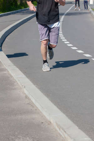 Runner's legs. The athlete runs along the city road. Muscle work. Close-up.