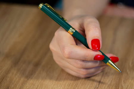 Beautiful female hand close up with red nails manicure write with pen Limited depth of field Close-upの写真素材