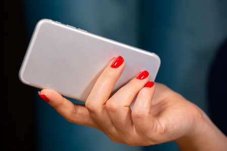 close-up, female hands with red manicure use a smartphone on a white background. Limited depth of...