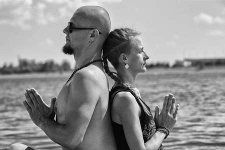 Man and pregnant woman are doing yoga on the beach Portrait