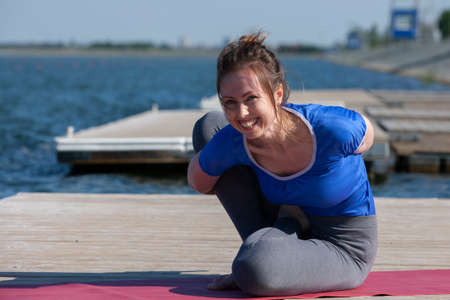 Young woman doing yoga in morning park near lake. Portrait