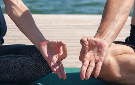 Attractive male and female practicing yoga in lotus pose close up hands. A young couple doing yoga to meditate their body and soul after work. Two people doing yoga outdoors. Portraitの写真素材