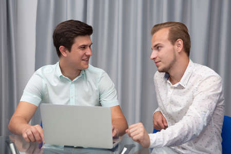 Two cheerful young businessmen working and using laptop on business meeting together. Portraitの写真素材