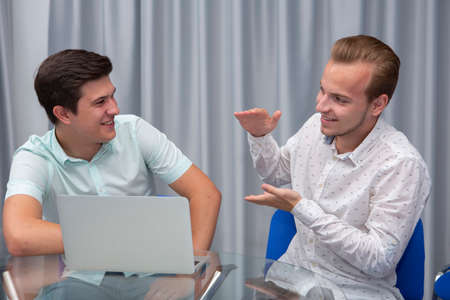 Two cheerful young businessmen working and using laptop on business meeting together. Portrait