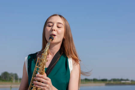 Beautiful smiling girl with saxophone. Young beautiful saxophonist with saxophone - outdoor in nature. Portraitの写真素材