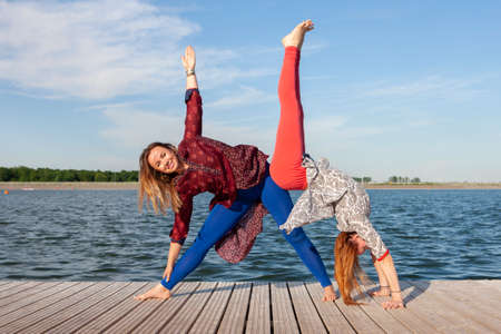 Two women exercising in the park. Young beautiful woman doing exercises together outdoors. Portraitの写真素材