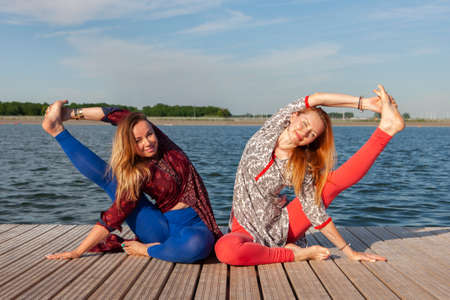 Two women exercising in the park. Young beautiful woman doing exercises together outdoors. Portraitの写真素材