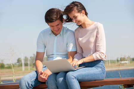Couple using a laptop outdoors and looking happy. Portrait.の写真素材