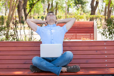 Young man with laptop sitting on a wooden bench. Portraitの写真素材