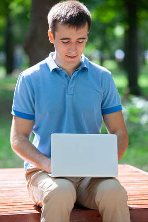 Young man with laptop sitting on a wooden bench. Portraitの写真素材