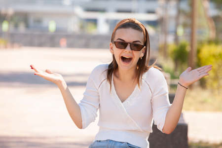 Cheerful girl making gun shot gesture. Beautiful young woman in casual enjoying leisure time in city park, turning round, smiling and gesturing at camera. Gesturing concept Portraitの写真素材