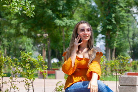 Close-up portrait of glamorous girl in glasses talking on phone. Outdoor portrait a blonde young woman talking by her smartphone and smiles.の写真素材