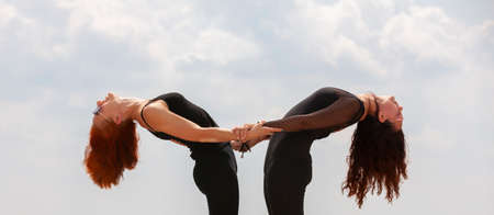 Two young Caucasian women yogi doing balance back stretch acro yoga pose. Women doing stretching workout in park outdoors at sunset. Healthy lifestyle modern activity. Portraitの写真素材