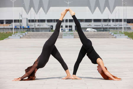 Two young Caucasian women yogi doing balance back stretch acro yoga pose. Women doing stretching...