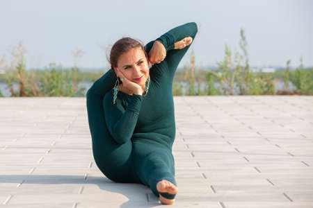 Thin brunette girl plays sports and performs beautiful and sophisticated yoga poses in a summer...