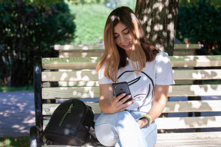 Young woman drinking coffee from paper cup. Sitting on bench in park. Portraitの写真素材