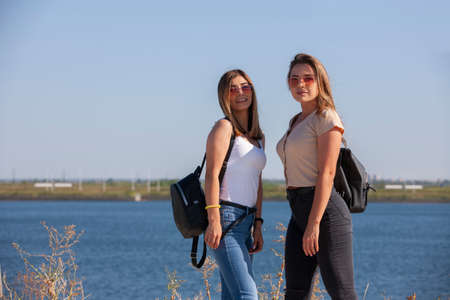 two beautiful young and stylish girl sitting in a summer city near water. Portrait.の写真素材