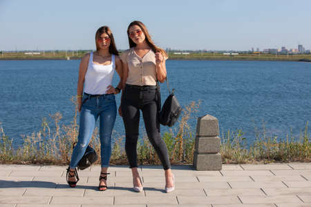 two beautiful young and stylish girl sitting in a summer city near water. Portrait.の写真素材