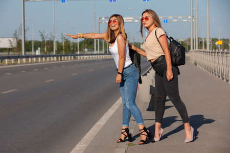 Two beautiful young women are hitchhiking on the road and try to find someone to take them to their hotel. Portrait.の写真素材