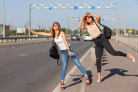 Two beautiful young women are hitchhiking on the road and try to find someone to take them to their hotel. Portrait.の写真素材