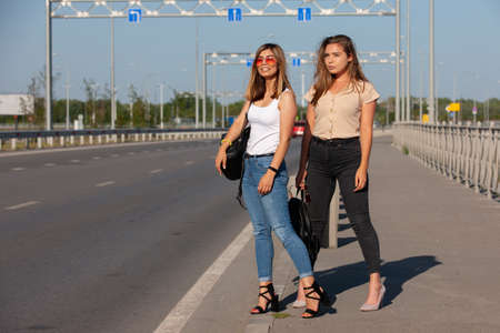 Two beautiful young women are hitchhiking on the road and try to find someone to take them to their hotel. Portrait.の写真素材