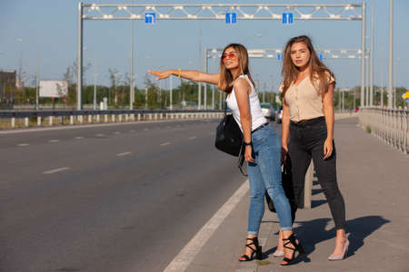 Two beautiful young women are hitchhiking on the road and try to find someone to take them to their hotel. Portrait.の写真素材