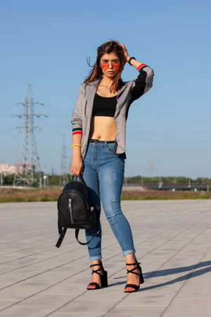 Happy joyful young woman posing by river and looking away. Portrait of cheerful lady in casual standing outside, keeping hands in jeans pocket and smiling. Outdoor portrait conceptの写真素材