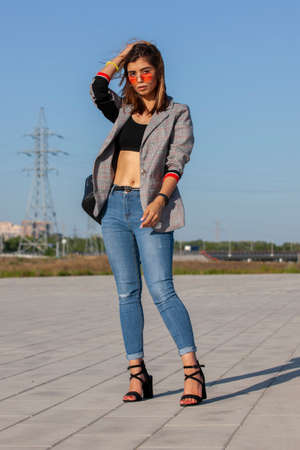 Happy joyful young woman posing by river and looking away. Portrait of cheerful lady in casual standing outside, keeping hands in jeans pocket and smiling. Outdoor portrait conceptの写真素材