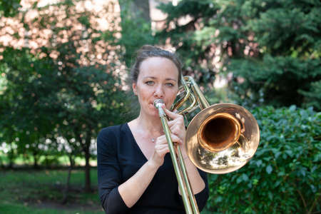 Girl learning to play trombone. Portrait of a girl on a background of a city park park. Portrait. Close-up.の写真素材