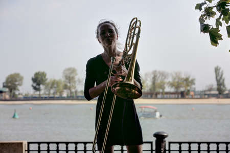 Girl learning to play trombone. Girl plays standing on the alley of a city park. Portrait.の写真素材