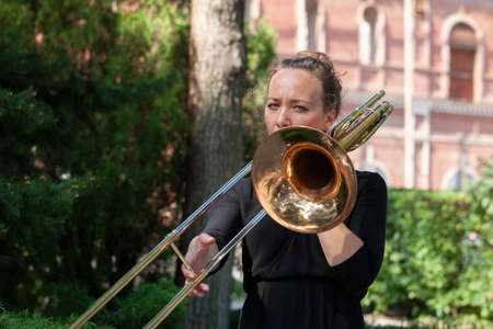Girl learning to play trombone. Portrait of a girl on a background of a city park park. Portrait. Close-up.の写真素材