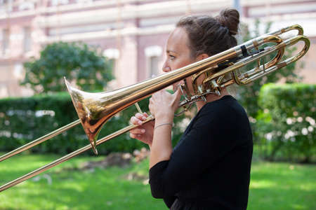 Girl learning to play trombone. Portrait of a girl on a background of a city park park. Portrait. Close-up.の写真素材