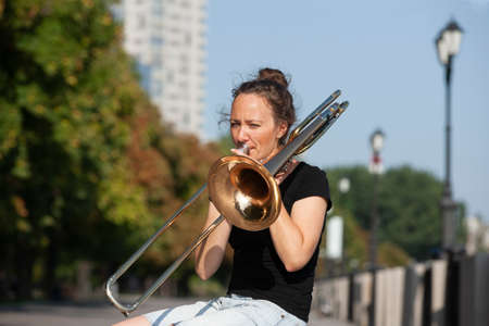 Girl learning to play trombone. Girl plays sitting on the promenade. Portrait.の写真素材