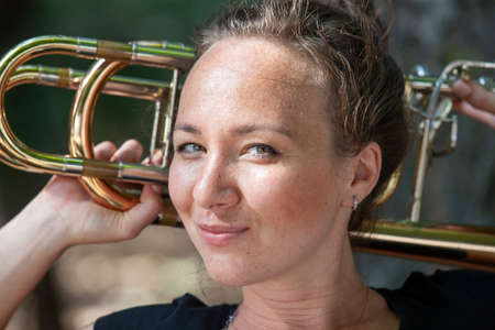 Girl learning to play trombone. Portrait of a girl on a background of a city park park. Portrait. Close-up.の写真素材
