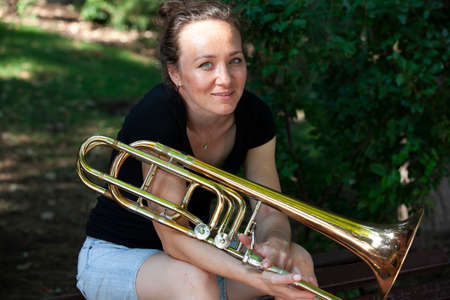 Girl learning to play trombone. Portrait of a girl on a background of a city park park. Portrait. Close-up.の写真素材