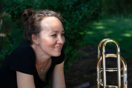 Girl learning to play trombone. Portrait of a girl on a background of a city park park. Portrait. Close-up.の写真素材