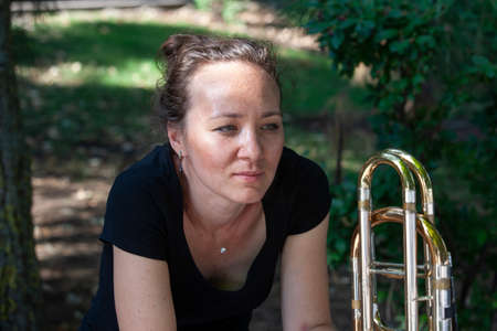 Girl learning to play trombone. Portrait of a girl on a background of a city park park. Portrait. Close-up.の写真素材