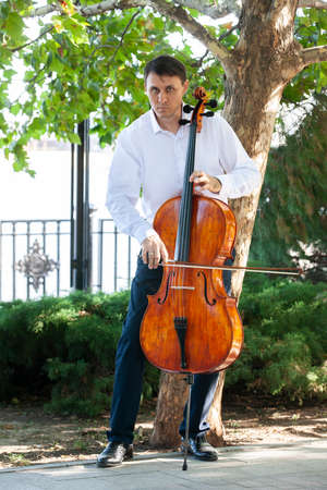 Street musician, young man playing cello in the street of big city, close up. Portrait.の写真素材