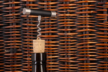 Opening a wine bottle with a cork screw in a restaurant. Against the background of a wicker basket of vines. Limited depth of field. Close-upの写真素材