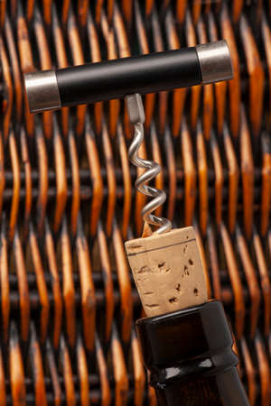 Opening a wine bottle with a cork screw in a restaurant. Against the background of a wicker basket...