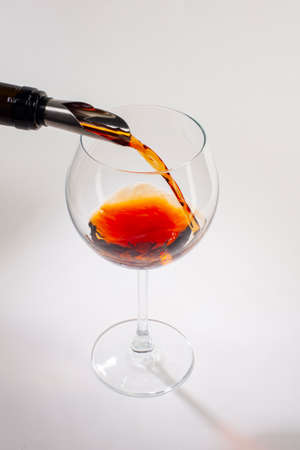 Pouring red wine into the glass. Glass of red wine on a white background and with soft shadow. Close-up.の写真素材