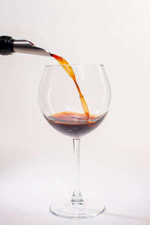 Pouring red wine into the glass. Glass of red wine on a white background and with soft shadow. Close-up.の写真素材