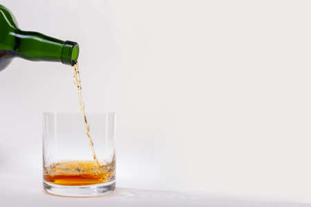 Close-up of an elegant glass for spirits, with a spilled liquor, similar to rum or whiskey, on a white background. There is a place for text. Limited depth of field.の写真素材