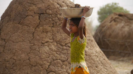 GWALIOR, INDIA - APRIL 17, 2016: An unidentified indian village girl carrying cow dung over her head.のeditorial素材