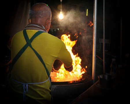 Chef cook making a show with flames while cooking in a night market.