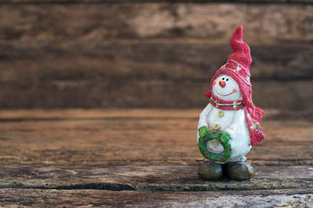 On the night of Christmas snowman standing on old wooden table. snowman holding a wreath .の写真素材