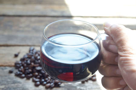 Hand holding a cup of coffee and coffee beans on a wooden tableの写真素材
