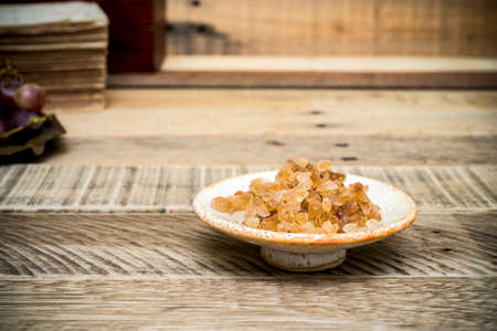 Crystalline organic brown rock sugar in ceramic bowl on wood table.の写真素材